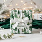Christmas gift wrapped in green watercolor pine tree paper with a white ribbon and "Season's Greetings" tag.