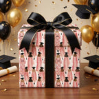 Pink graduation wrapping paper with graduate illustrations and a black satin bow by Wrapped Studios.
