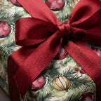 Christmas gift box with watercolor ornament wrapping paper and a red satin bow.