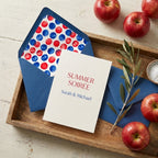 Summer soirée invitation with red and blue polka dot envelope on a wooden tray by Wrapped Studios.