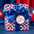 Red and blue polka dot birthday wrapping paper with a blue satin bow and gift tag by Wrapped Studios.