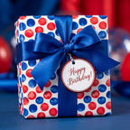 Red and blue polka dot birthday wrapping paper with a blue satin bow and gift tag by Wrapped Studios.