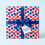 Red and blue polka dot birthday wrapping paper on a gift box with a satin bow by Wrapped Studios.