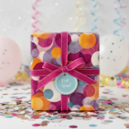 Festive birthday wrapping paper with colorful circles, pink ribbon, and "For You!" tag surrounded by confetti.