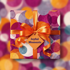 Square gift wrapped in colorful modern circle pattern paper with orange satin ribbon and "Joyful Moments" tag.