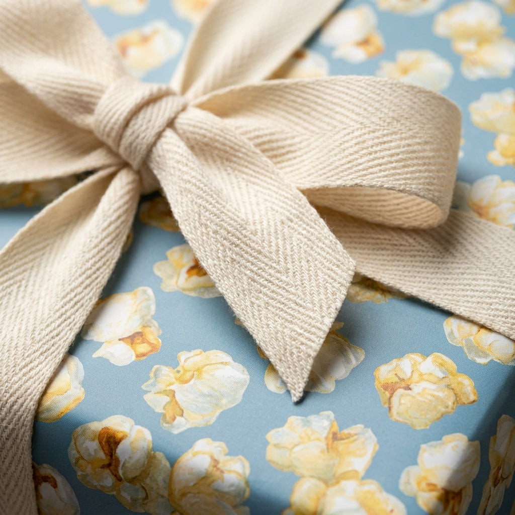Whimsical popcorn wrapping paper in blue, tied with a cream herringbone ribbon bow by Wrapped Studios.