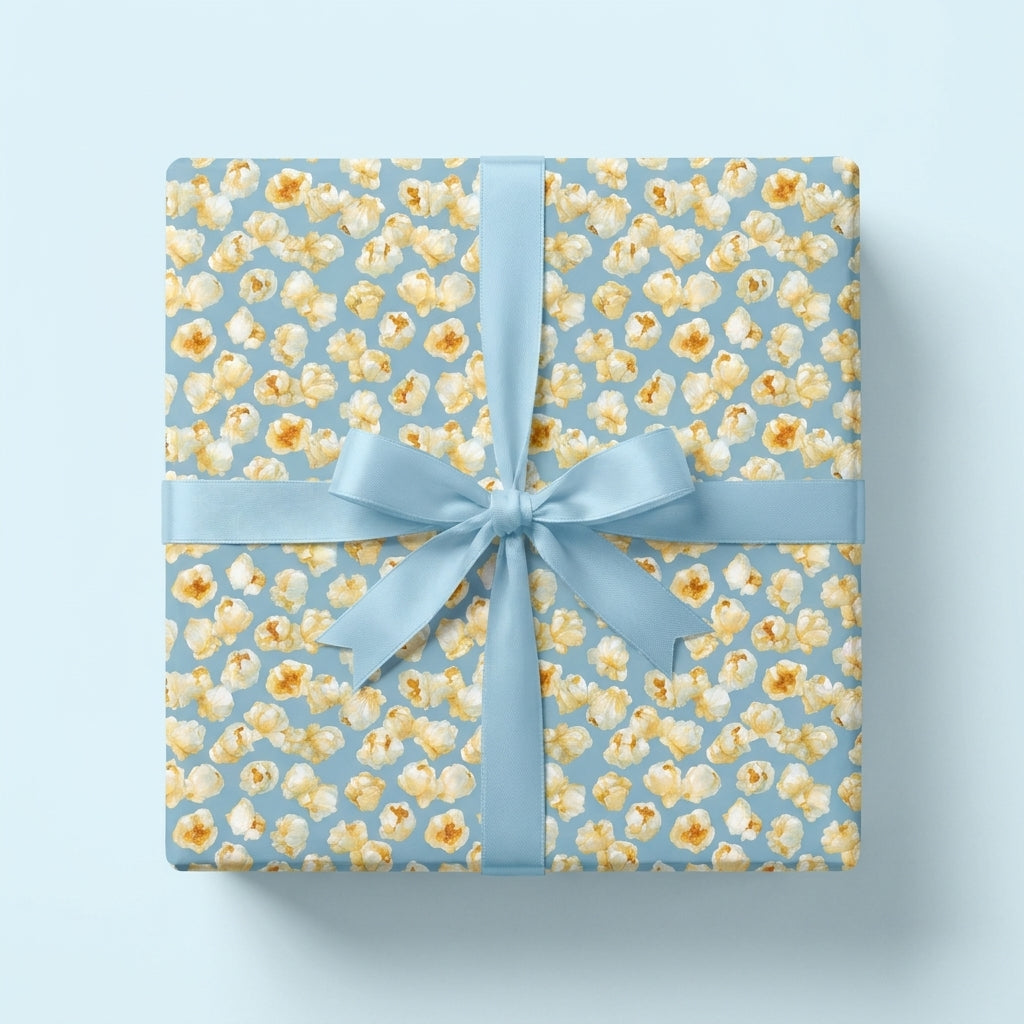 Popcorn birthday wrapping paper with a light blue satin ribbon on a gift box, by Wrapped Studios.