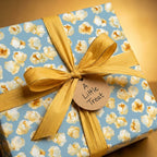 Cute popcorn wrapping paper on a blue gift box with a gold bow and treat tag by Wrapped Studios.