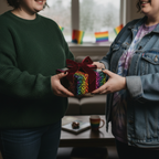 Person giving a gift wrapped in colorful, rainbow-patterned paper with a velvet bow.