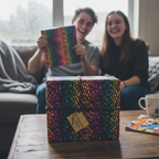 A gift wrapped in colorful raindrop pattern wrapping paper, with teens celebrating.