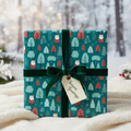 Festive Christmas wrapping paper with a playful Santa, red and teal trees, dark green velvet ribbon, and a "Season's Greetings" tag.