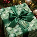 Luxury green Christmas wrapping paper with ornament pattern, satin bow, and tag by Wrapped Studios.