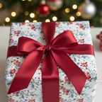 Festive holiday wrapping paper with a red berry and leaf pattern, tied with a luxurious deep red ribbon and bow, set against a blurred Christmas tree.