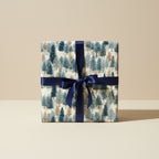 Square gift box wrapped in modern blue tree print Christmas wrapping paper with a navy satin ribbon.