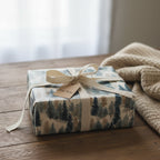Rustic gift wrapped in woodland tree wrapping paper with tan ribbon on a wooden table.