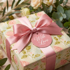 Floral wrapping paper by Wrapped Studios on a gift box with a pink satin ribbon bow and 'With Love' tag.