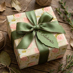 Elegant floral wrapping paper with a sage green ribbon on a rustic gift box, by Wrapped Studios.
