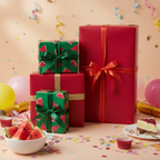 Festive birthday gift wrap featuring bold red and playful watermelon print boxes with ribbons, balloons, and cake on a peach background.