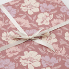 Elegant floral wrapping paper in mauve, lavender, and cream, tied with a simple white satin ribbon.