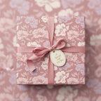 Elegant floral wrapping paper in mauve and cream, tied with a satin ribbon and gift tag.
