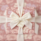 Elegant floral wrapping paper in mauve with a soft white ribbon bow and gift tag.