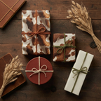 Rustic gift wrap assortment featuring cowhide-print and solid-color paper, tied with twine, on a dark wood surface with wheatgrass accents.