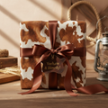 Western-style gift wrap: brown and white cowhide print wrapping paper with brown ribbon and "Yeehaw & Howdy!" tag.