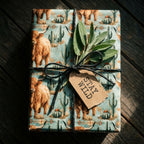 Rustic highland cow wrapping paper with cactus print on a gift box by Wrapped Studios.