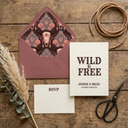 Boho western wedding invitation suite with bull skull envelope liner by Wrapped Studios on rustic wood.