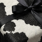 Black and white cow print wrapping paper with a satin ribbon bow on a wrapped gift.