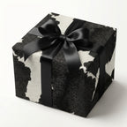 Cow print wrapping paper with black satin ribbon on a square gift box.