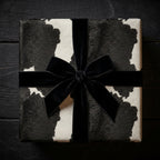 Square gift wrapped in cow print wrapping paper with a black velvet ribbon and bow.