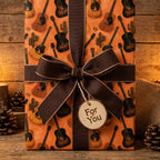 Rustic acoustic guitar wrapping paper with a brown ribbon bow and wood tag by Wrapped Studios.