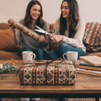 Rustic gift with patterned wrapping paper and leather bow, two women cutting matching paper in background.