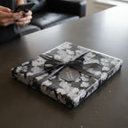 Square gift wrapped in black floral wrapping paper with a charcoal ribbon and tag.