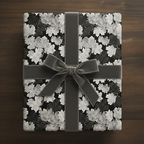 Elegant gift wrapped in black floral wrapping paper with a gray velvet ribbon on a wood surface.