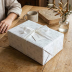 Baptism wrapping paper with a grey cross pattern, white ribbon, and gift tag by Wrapped Studios.