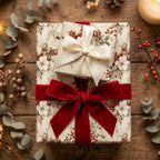 Elegant floral wrapping paper with red velvet ribbon and cream bow on a rustic wood surface.