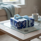 Elegant gift wrapped in navy floral wrapping paper with light blue ribbon on a glass-topped table.