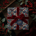 Luxury botanical Christmas wrapping paper with a red velvet bow and gift tag, by Wrapped Studios.