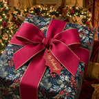 Navy botanical Christmas gift wrap with a large red bow and 'No Peeking' tag by Wrapped Studios.