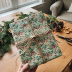 Rustic Christmas gift wrap featuring red berries and green leaves tied with natural twine.
