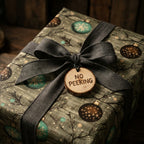 Rustic Christmas wrapping paper with ornaments, charcoal bow, and wood tag by Wrapped Studios.