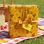 Gift wrapped in yellow floral wrapping paper with gold ribbon, picnic setting.