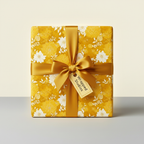 Square gift box in mustard yellow floral wrapping paper with gold ribbon bow.