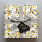 Luxury Christmas gift wrap with yellow ornaments and a grey velvet bow by Wrapped Studios.